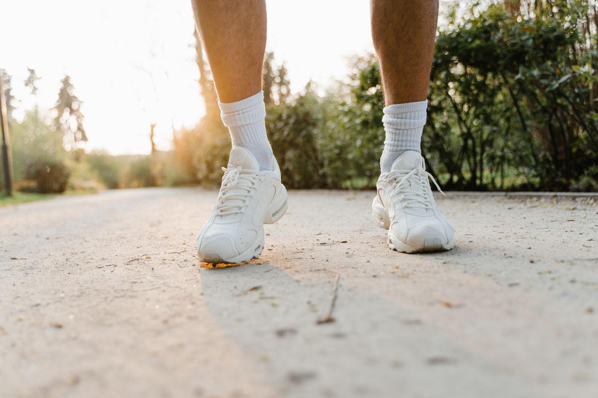 White walking shoes mid-stride on a paved park path