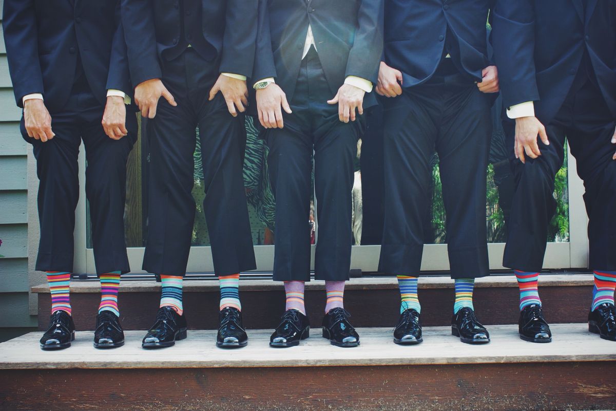 Groomsmen in dark suits lifting their trousers to show their socks and dress shoes